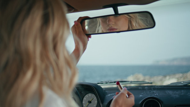 坐在车里调整后视镜的女孩拿着红色的口红特写图片下载