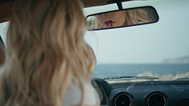 涂着口红的漂亮女人看着汽车后视镜。唇妆图片下载