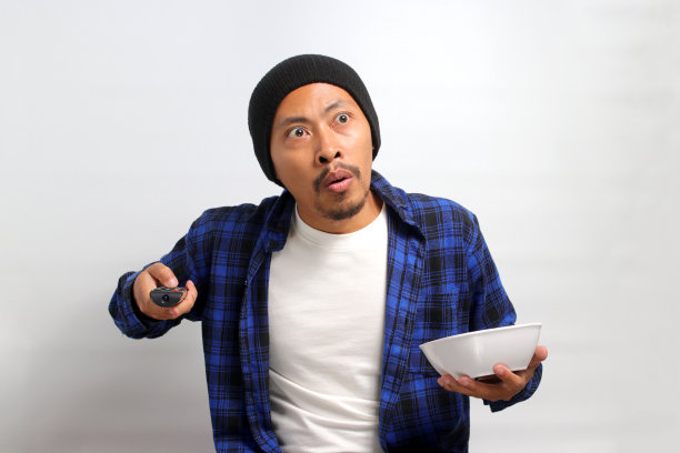 一名亚洲男子拿着电视遥控器暂停视频图片下载