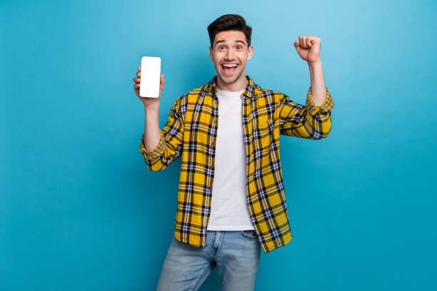 照片中，一个欣喜若狂的家伙沉迷于用智能手机玩电子竞技投注，在蓝色的背景下，他举起了拳头图片下载