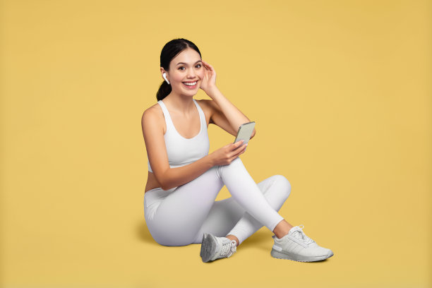 微笑的女人穿着运动服，黄色背景上戴着手机和耳机图片下载