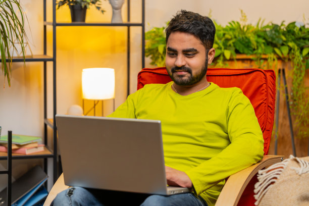 年轻的自由职业者坐在椅子上工作的笔记本电脑浏览互联网在家里的客厅图片下载