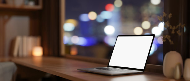 靠窗的木桌上放着一台笔记本电脑模型，窗外是城市夜景。图片下载