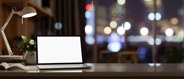 夜晚在黑暗房间里的现代办公桌，笔记本电脑模型和城市夜灯在窗户上。图片下载