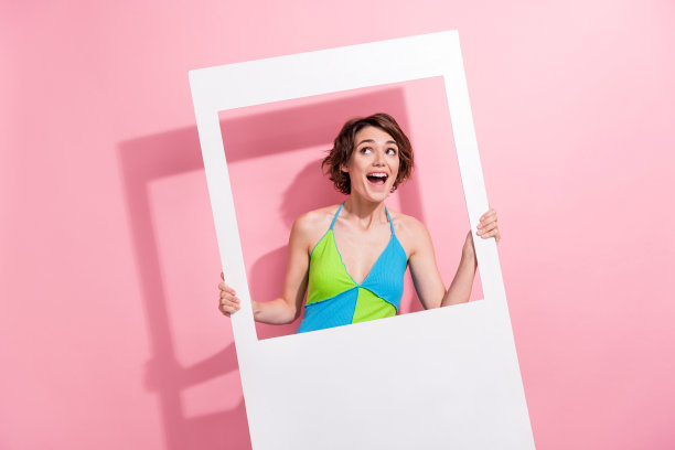 照片时髦兴奋的女士穿着绿色的蓝色背心拿着纸相框看空空间孤立的粉红色背景图片下载