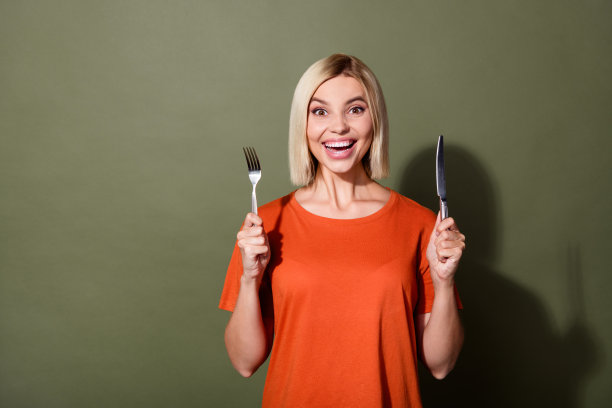 照片肖像年轻的鲍勃金发女子穿着橙色t恤惊讶地拿着餐具准备吃孤立的卡其色背景图片下载