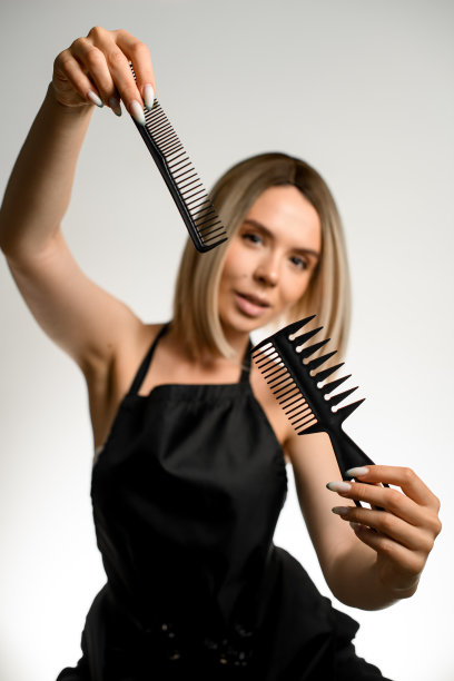 穿着黑色围裙的金发女发型师在白色背景上展示各种专业梳子图片下载