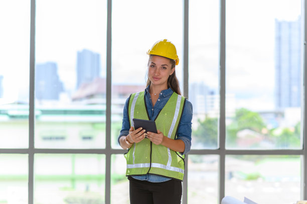 工地上戴着黄色安全帽的女建筑工程师手持平板电脑的照片。图片下载