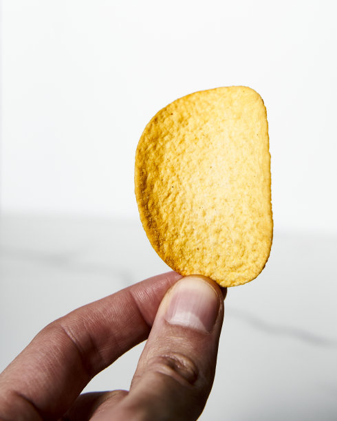 男人手里拿着白色大理石背景上的金黄色脆皮薯片。极简的食物照片。图片下载