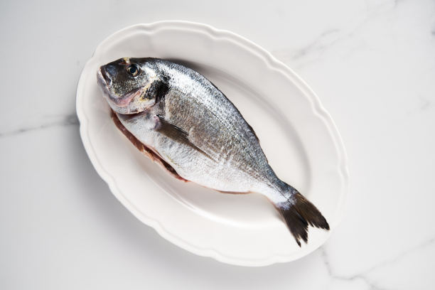 白色大理石背景白色盘子上的新鲜生鲷鱼。简约食物照片。地中海饮食。顶部视图留白图片下载
