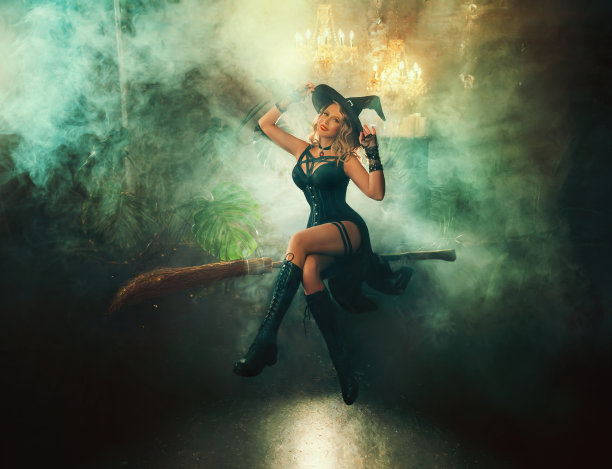 艺术照片真人悬浮性感女巫女人坐在飞天扫帚在空气中黑暗的房间充满烟雾。快乐的脸幻想女孩巫师魔术师仙女的风格。黑色哥特式服装万圣节服装帽子图片下载