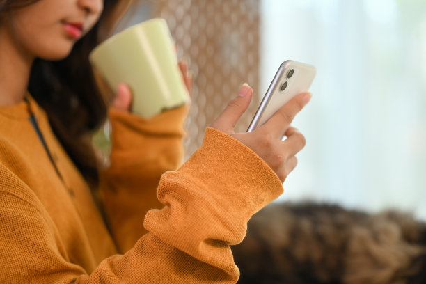 照片中年轻女子一边喝茶一边看手机短信。图片下载