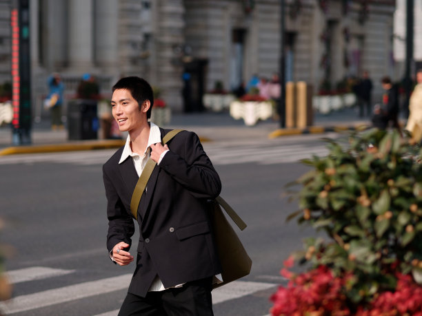 英俊的中国年轻人的肖像，黑色短发，穿着黑色运动夹克，在阳光明媚的冬日穿过现代城市建筑背景的街道，男性时尚，酷的亚洲年轻人。图片下载