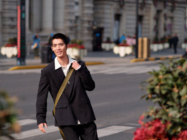 英俊的中国年轻人的肖像，黑色短发，穿着黑色运动夹克，在阳光明媚的冬日穿过现代城市建筑背景的街道，男性时尚，酷的亚洲年轻人。图片下载