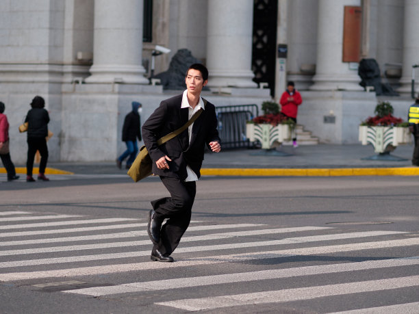 英俊的中国年轻人的肖像，黑色短发，穿着黑色运动夹克，在阳光明媚的冬日穿过现代城市建筑背景的街道，男性时尚，酷的亚洲年轻人。图片下载