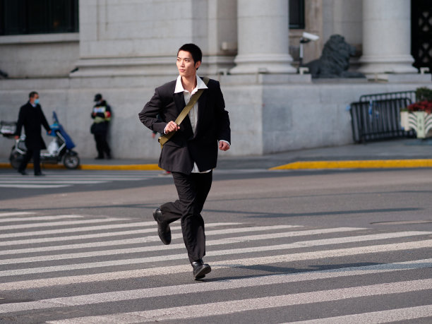 英俊的中国年轻人的肖像，黑色短发，穿着黑色运动夹克，在阳光明媚的冬日穿过现代城市建筑背景的街道，男性时尚，酷的亚洲年轻人。图片下载