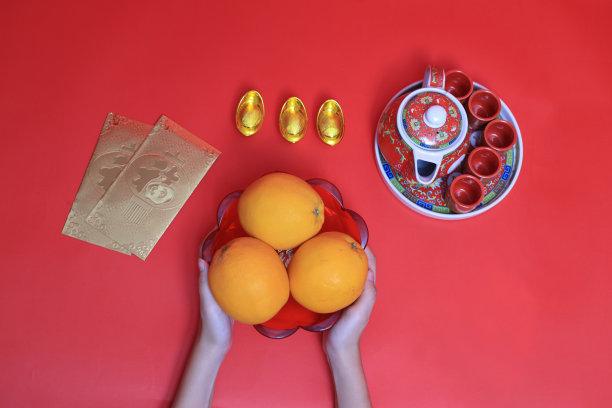 十几岁的女孩手里拿着橘子，还有茶具、金元宝和红色背景的金信封。中文字母的意思是富有和幸运图片下载