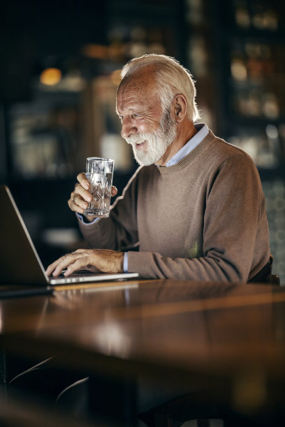 一个快乐的休闲高管正在用笔记本电脑做一个项目，在咖啡馆里喝水。图片下载