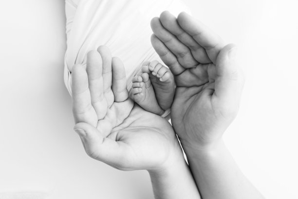 爸爸的手掌，妈妈都抱着刚出生的婴儿的脚。新生儿的脚放在父母的手掌上。工作室微距黑白照片的一个孩子的脚趾，脚跟和脚。图片下载