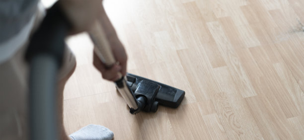 这张照片拍摄了一个人用现代家用吸尘器清洁硬木地板的特写镜头，重点是家务的效率。图片下载