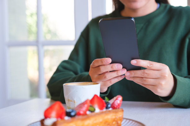 一名年轻女子手持并使用手机的特写照片，桌上放着咖啡杯和蛋糕图片下载