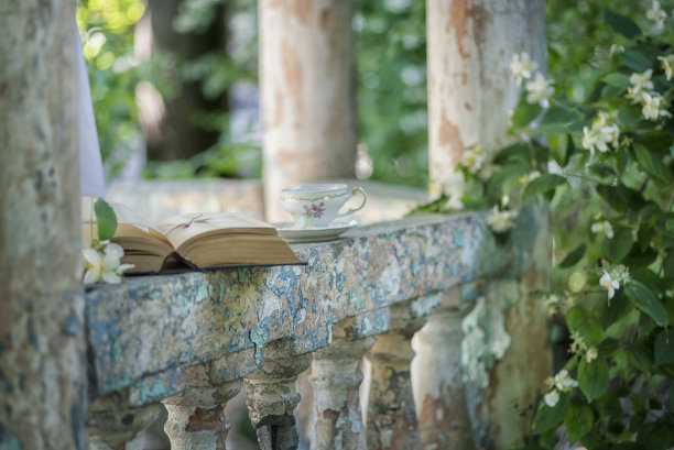 复古的照片。复古风格的茶水服务，在花园里茉莉花丛中，一个古老的巴洛克式凉亭的栏杆上放着一本书。图片下载