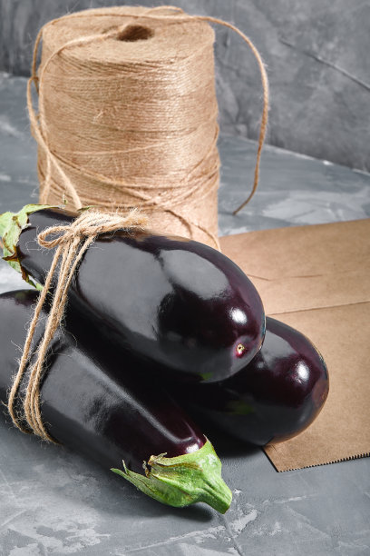 茄子在灰色的背景上，后面是纸袋和石南为包装。蔬菜配送，照片为网上商店配送。图片下载