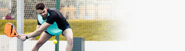 一个成年男子在室外球场打球拍网球的全景照片。这个男孩准备在下面击球。照片的右侧是空白的，用于广告文案或广告版面。图片下载