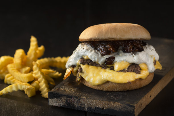 快餐，汉堡，奶油面包，切达奶酪，红肉和焦糖洋葱配蛋黄酱，深色背景，质朴的木头，正面照片配薯条图片下载