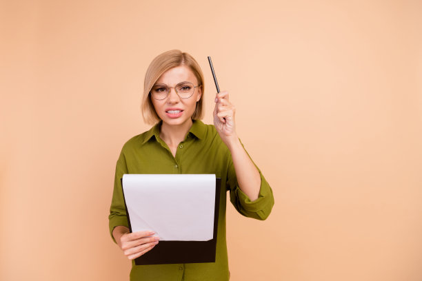 照片中，愤怒严厉的女人留着波波头，穿着绿色衬衫，戴着眼镜，拿着写字板，举起钢笔，孤立在米色背景上图片下载