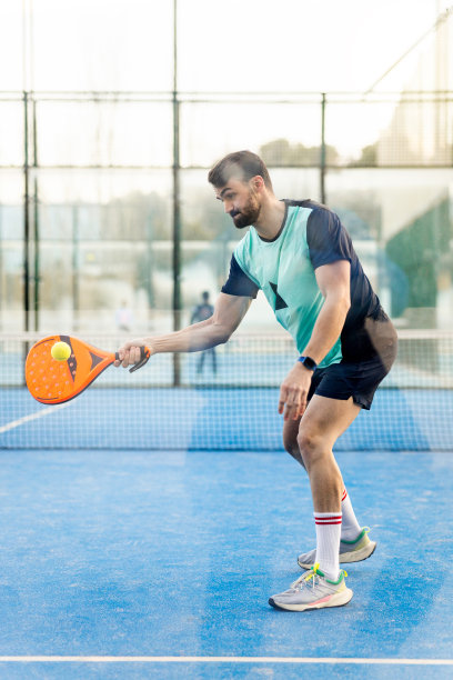 一名成年男子在户外场地玩打板游戏的垂直照片。这个男孩正在把球打在透明的墙上做一个反弹。男人玩板的概念。图片下载