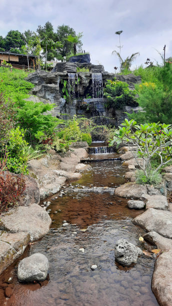有瀑布和河流的花园设计。河流周围有天然石墙和绿色植物的人工瀑布。人造森林。图片下载