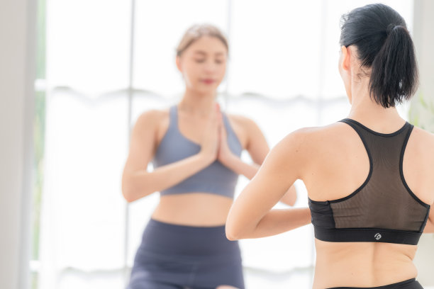 两个女人自信地练习瑜伽。穿着运动服的运动女性在家里的客厅里做健身伸展运动。运动和娱乐的概念。瑜伽老师正在帮助年轻女子。图片下载