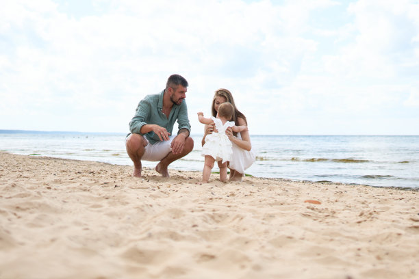 一对快乐的父母和他们一岁的女儿在海滩附近的沙滩上玩耍的照片图片下载