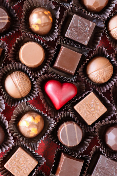 整幅图片的批量个人，情人节巧克力松露和果仁糖在纸盒，红色心形糖果，牛奶和黑巧克力，斑驳的红色背景，抬高视图图片下载