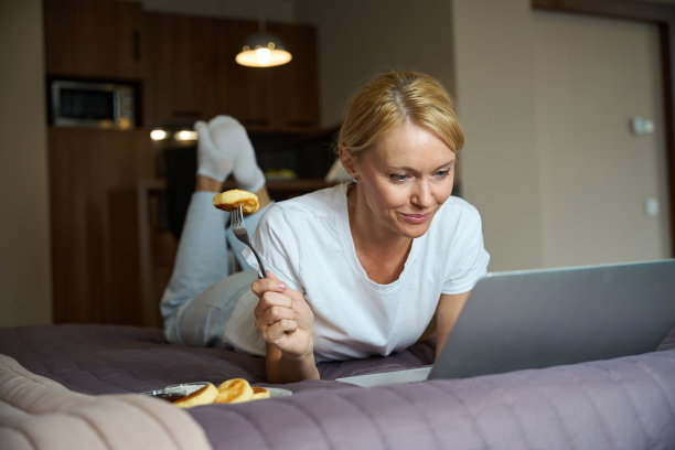 女性在卧室吃早餐时在电脑显示器上看东西图片下载