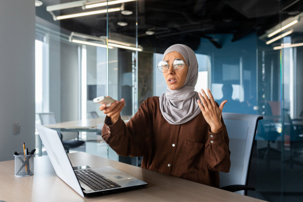 一位戴着头巾的年轻穆斯林女商人，在办公室里用笔记本电脑工作，用遥控器打开冷空调，感受热量，挥手图片下载