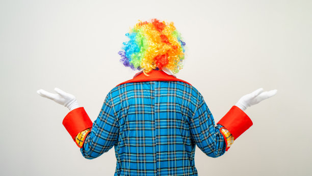 后视镜小丑先生。后面是滑稽的喜剧演员脸的肖像，小丑穿着彩色制服，戴着假发站着。在孤立的背景上摆出各种姿势的快乐表情男呆子。图片下载