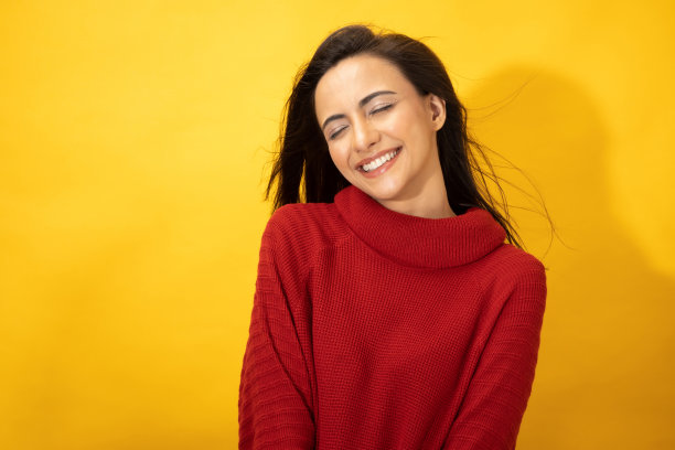 照片的年轻妇女在冬天穿站在黄色背景股票照片图片下载