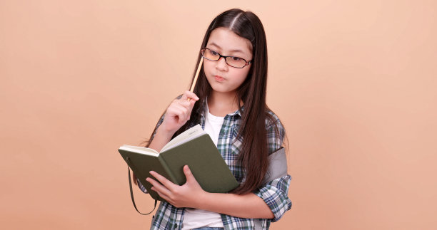 一个女学生在想什么并把它记在笔记本上。孤立在褐色背景的工作室。图片下载