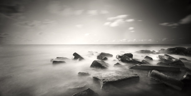 使用长曝光技术拍摄的黑白照片，描绘了淹没在海中的方形岩石。库存图片图片下载