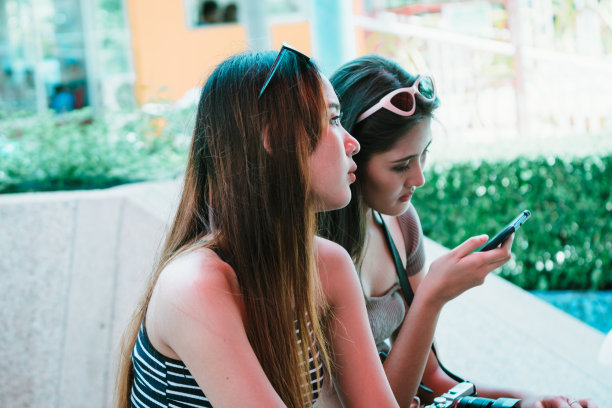 亚洲游客和朋友坐在一起，而她的朋友在看智能手机上的照片图片下载