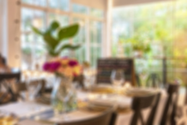 模糊背景的餐桌设置与鲜花和玻璃器皿在餐厅与散景光的背景使用。图片下载