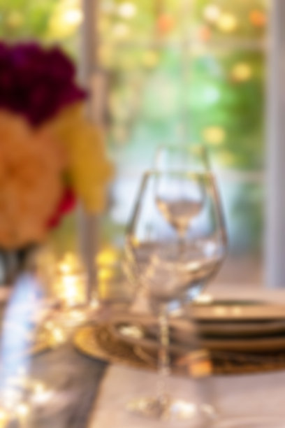 模糊背景的餐桌设置与鲜花和玻璃器皿在餐厅与散景光的背景使用。图片下载
