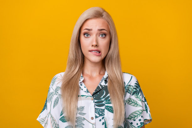 照片中，一头直发，穿着时尚印花衬衫的漂亮女人，在黄色背景上咬着嘴唇图片下载