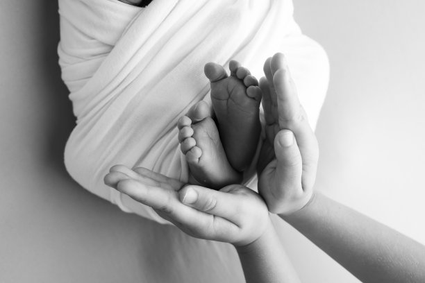 爸爸的手掌，妈妈都抱着刚出生的婴儿的脚。新生儿的脚放在父母的手掌上。工作室微距黑白照片的一个孩子的脚趾，脚跟和脚。图片下载