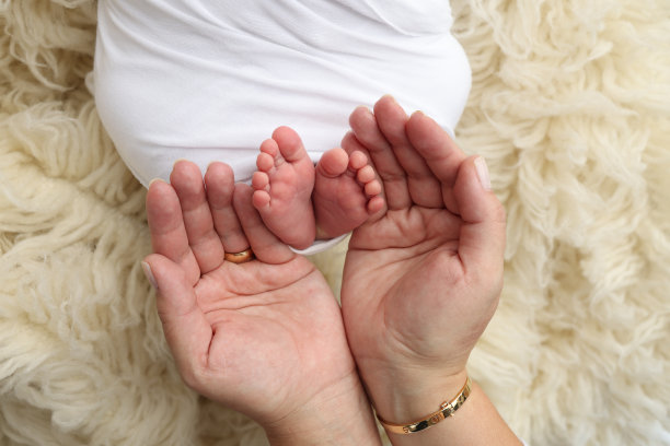 爸爸的手心，妈妈的脚上都抱着刚出生的婴儿的白毯子。新生儿的脚放在父母的手掌上。工作室微距照片的一个孩子的脚趾，脚跟和脚。图片下载