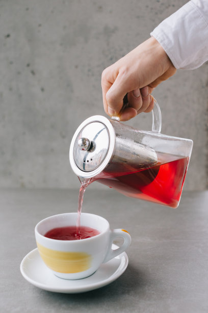 咖啡师的手将芳香的茶倒入杯中，在灰色的背景中孤立。图片下载