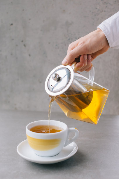 咖啡师的手将芳香的茶倒入杯中，在灰色的背景中孤立。图片下载