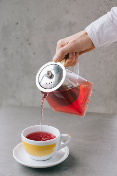 咖啡师的手将芳香的茶倒入杯中，在灰色的背景中孤立。图片下载